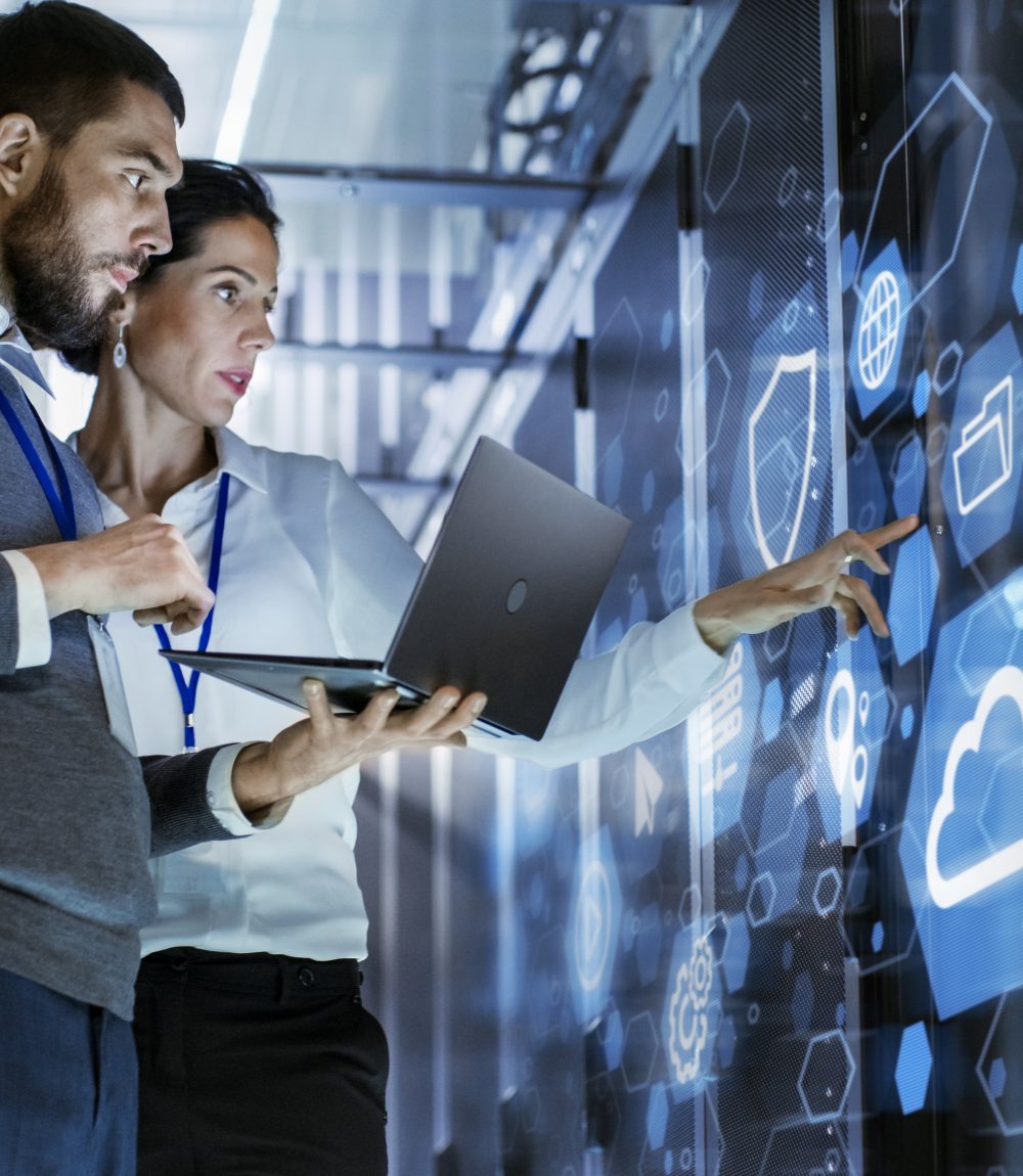 Male IT Specialist Holds Laptop and Discusses Work with Female Server Technician. They're Standing in Data Center, Rack Server Cabinet with Cloud Server Icon and Visualization.